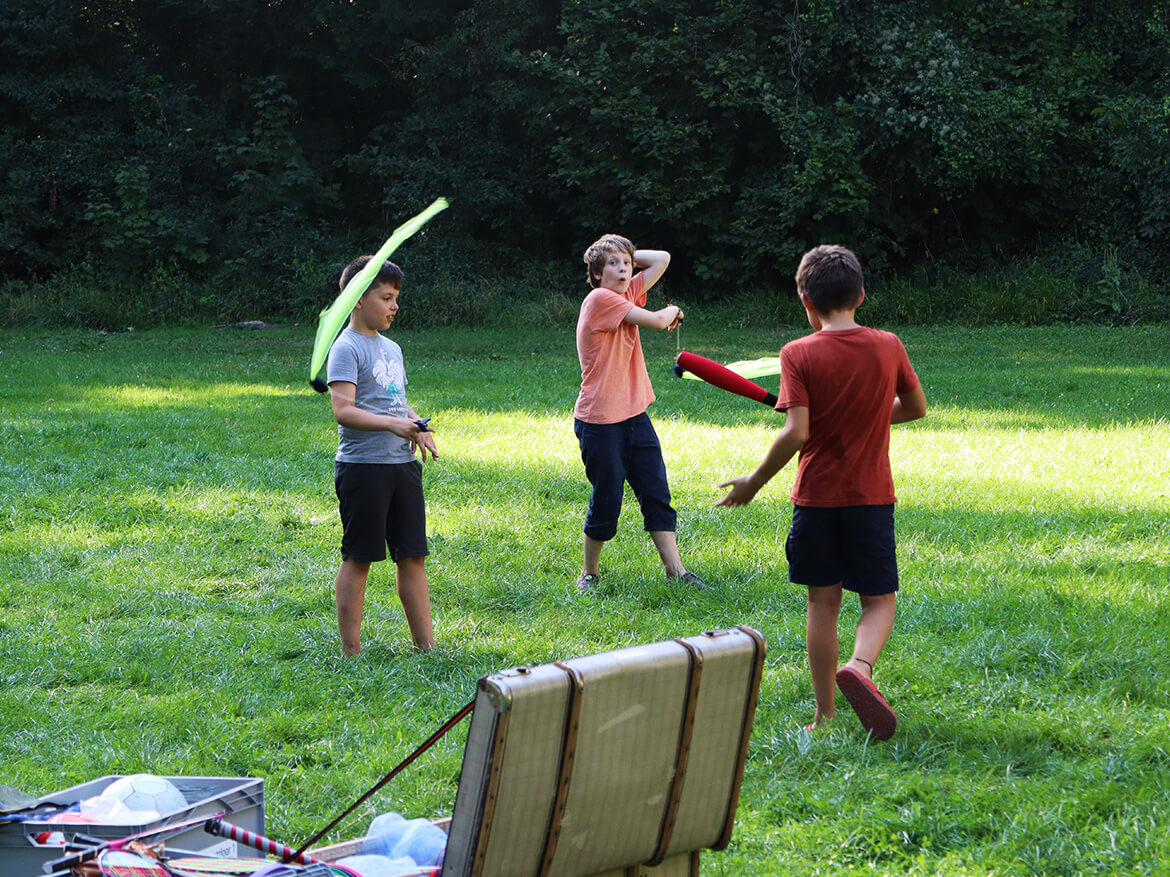 Drei Jungs spielen auf einer Wiese mit Jonglier-Gerätschaften