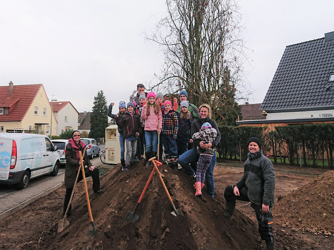 Auf einem großen Erdhügel steht stolz eine Gruppe Kinder mit ihren Eltern