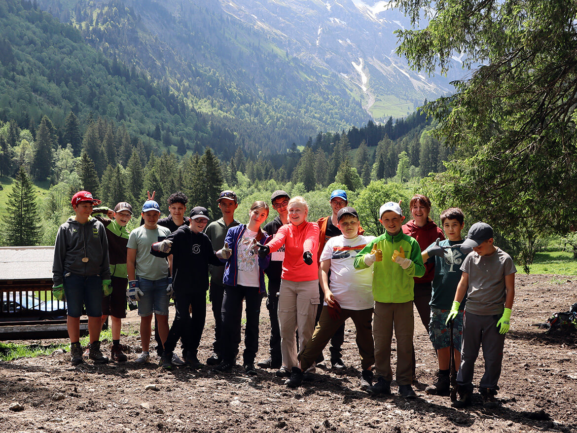 Eine Gruppe Kinder und Jugendlicher unterschiedlichen Alters posieren für ein Gruppenfoto vor einem beeindruckenden Alpenausblick