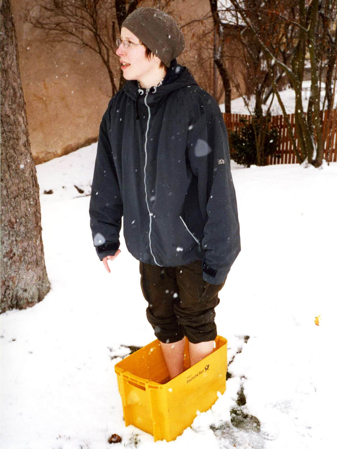 Stefanie steht barfus in einer gelben DHL-Post-Box, die warmes Wasser enthält, um sie herum liegt Schnee